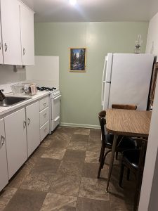 Interior view of a small, clean kitchen with white cabinets and a dining table.